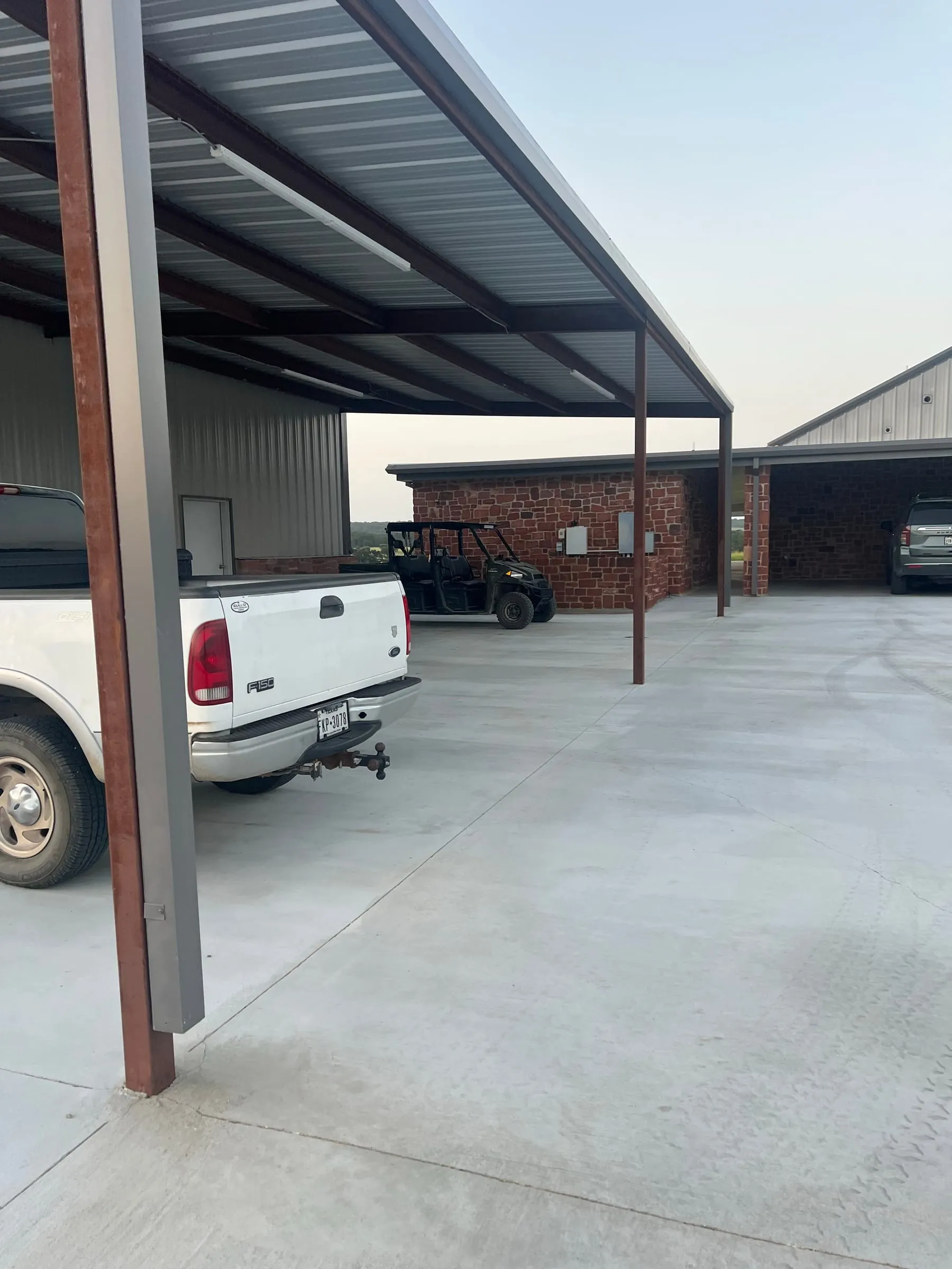 Steel-framed covered parking beside the metal building and stone-clad adjoining walls.