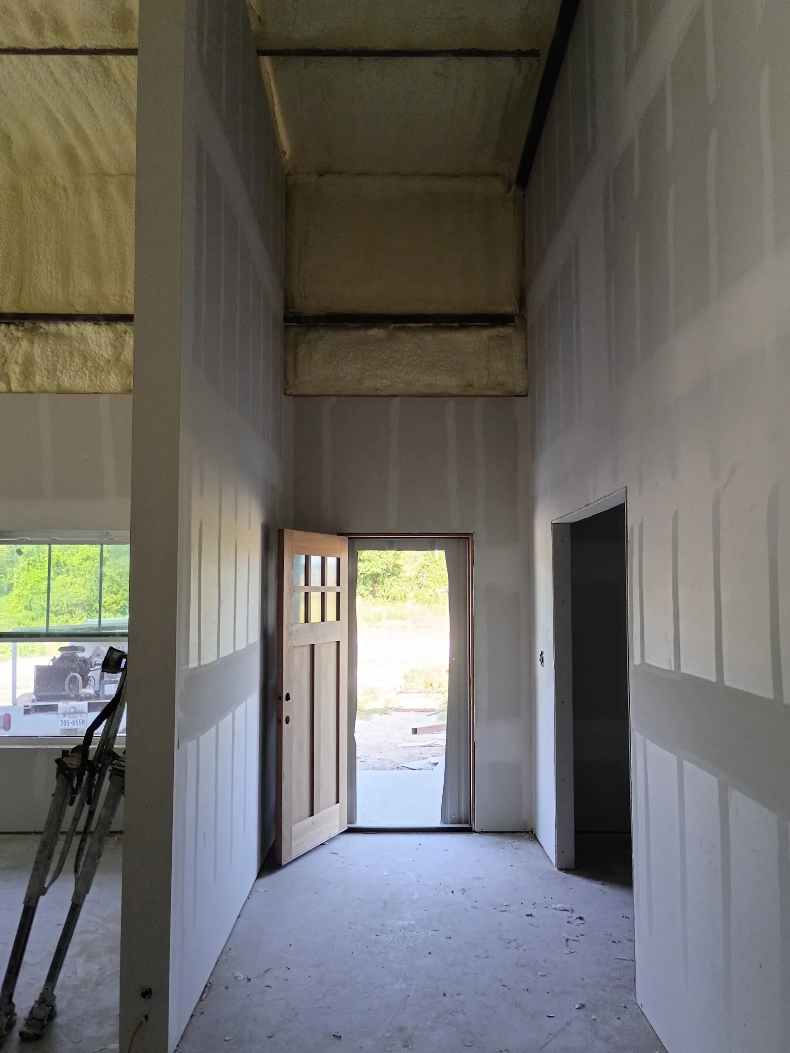 Tall entry hall with drywall installed around the barndominium's wood front door.