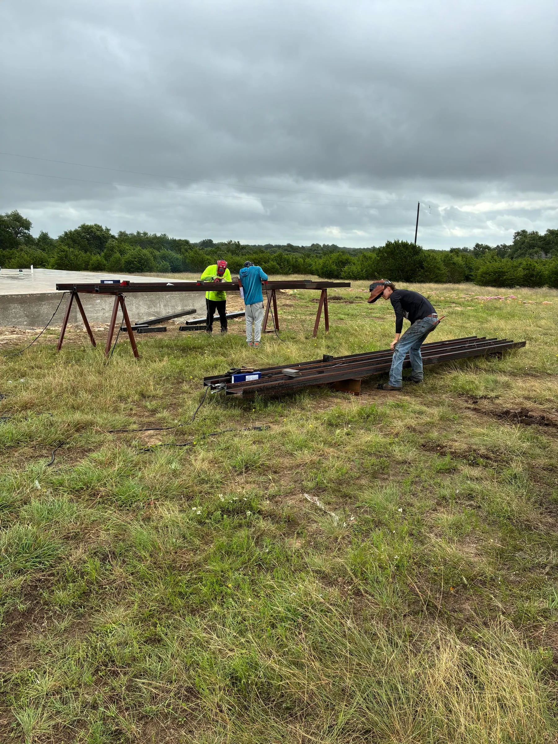 Crew staging long steel members beside the prepared foundation.