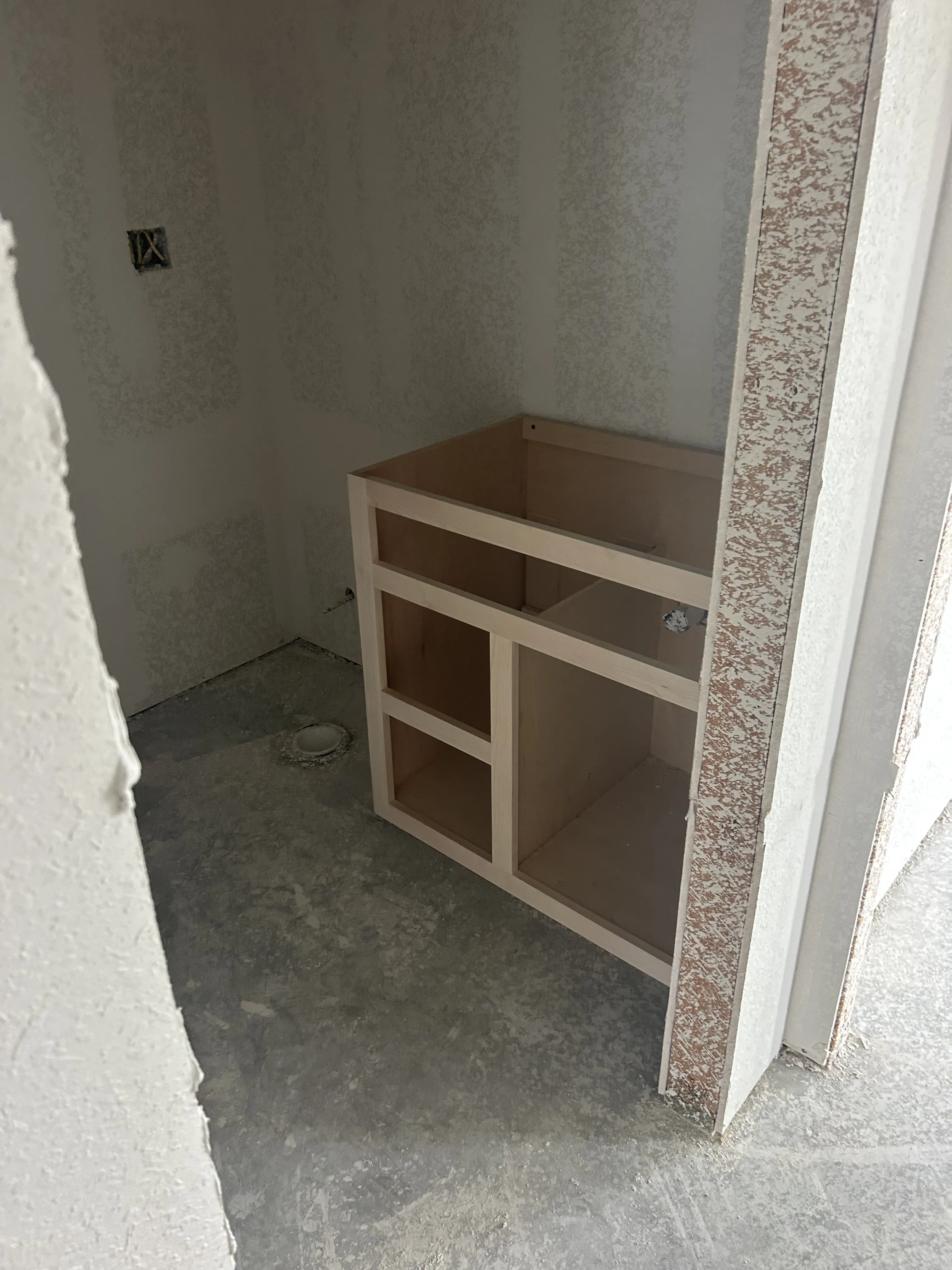 Small custom vanity cabinet installed in an unfinished bathroom alcove.