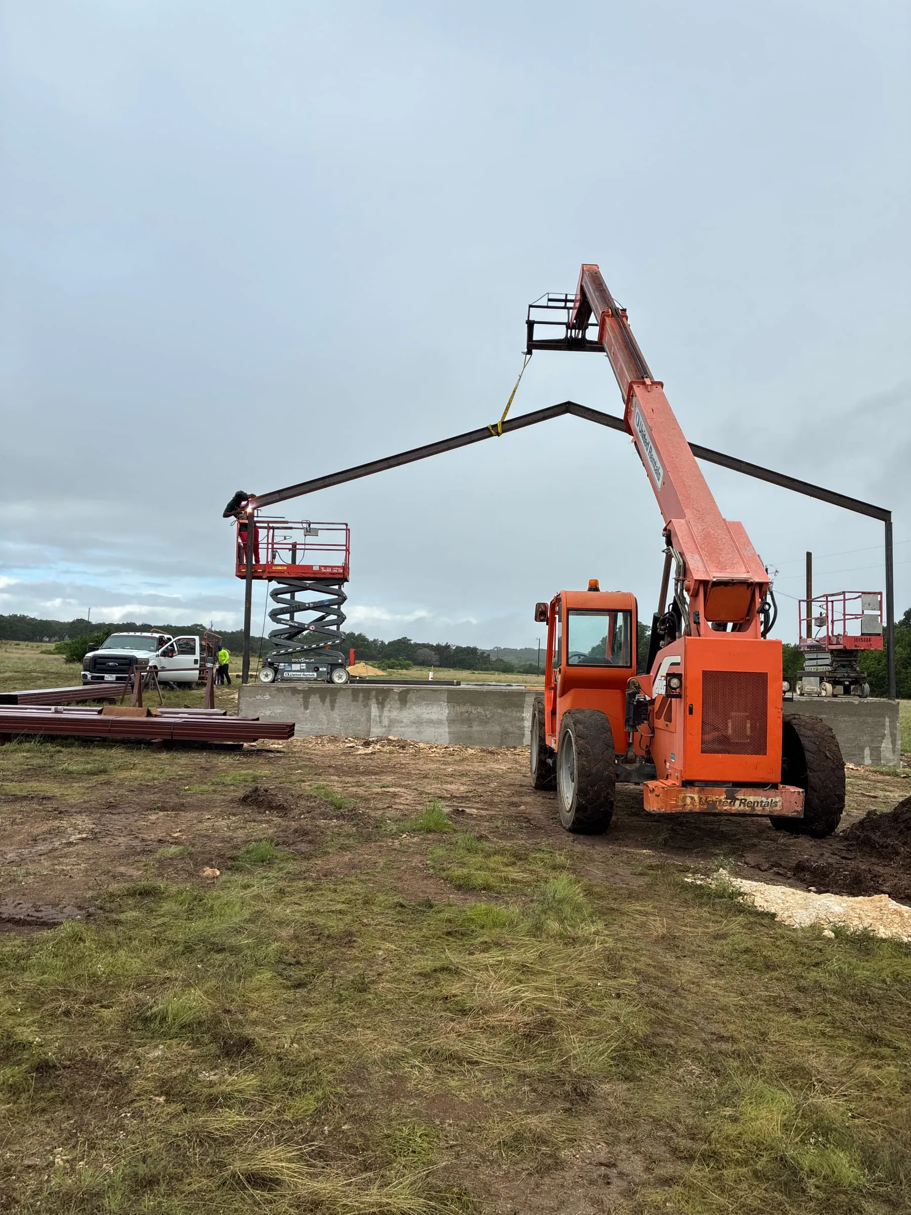 Crews use lifts and a telehandler to set a roof beam in place.