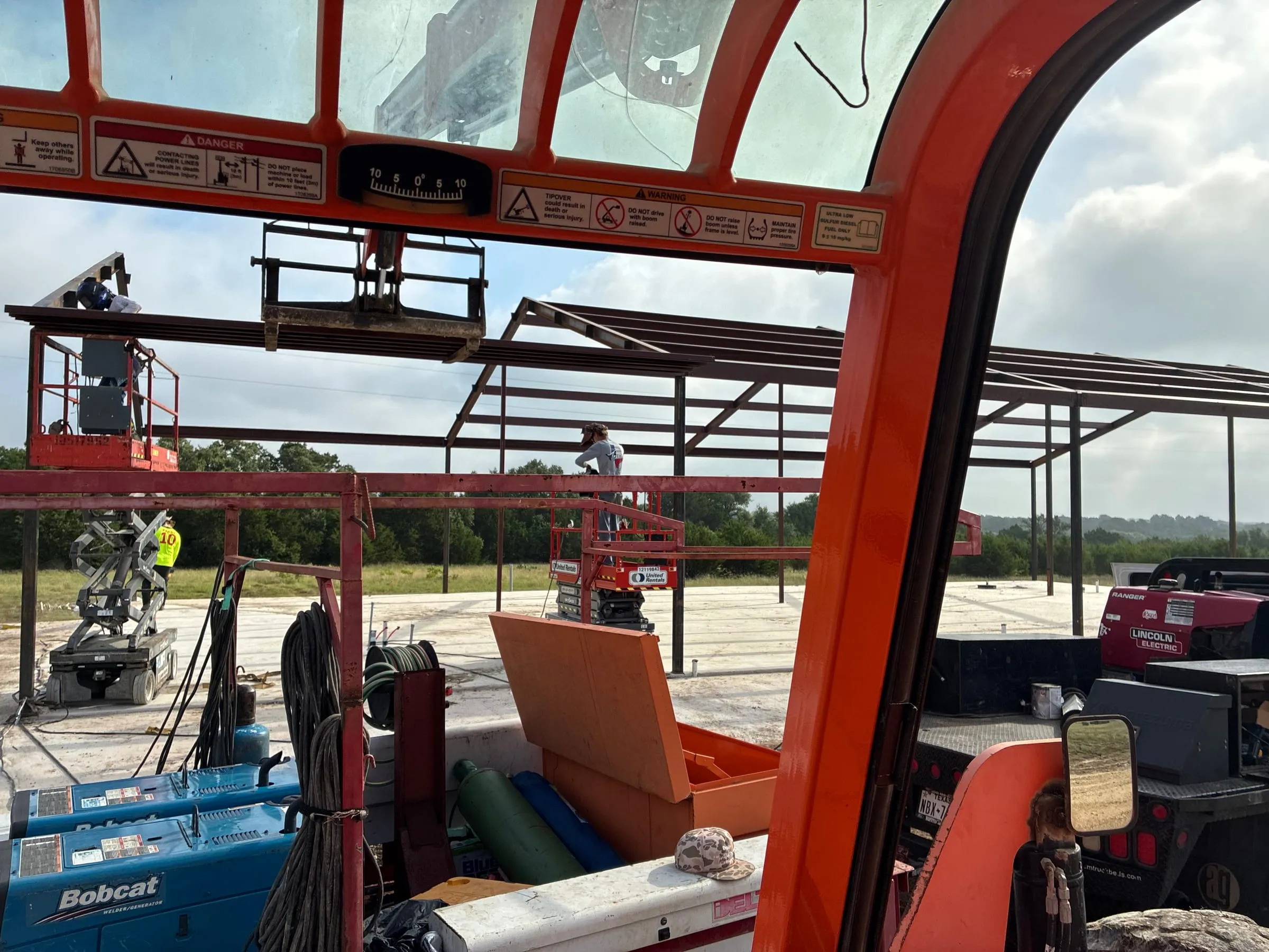 View through the telehandler cab toward the growing steel frame.