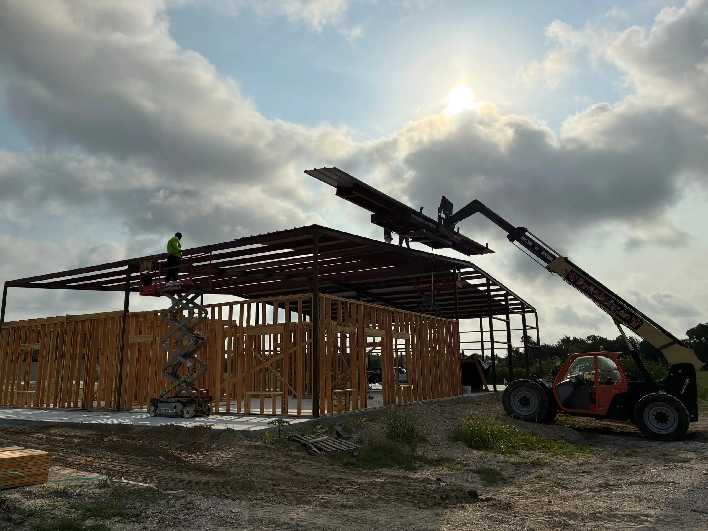 Telehandler lifts bundles of metal roof panels to the crew above.