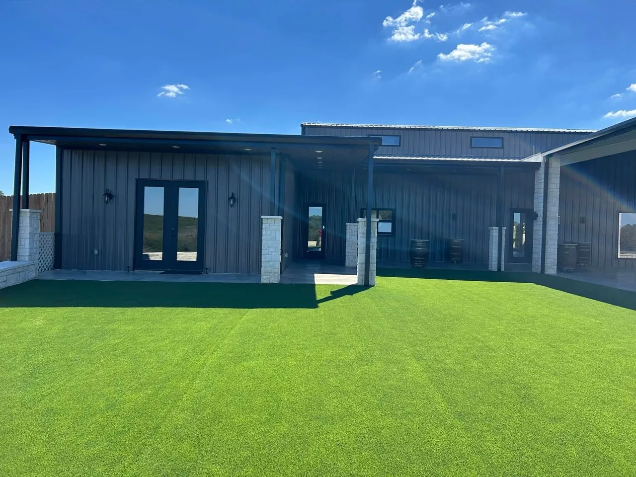 A completed metal home with a covered courtyard, stone columns, and green lawn.
